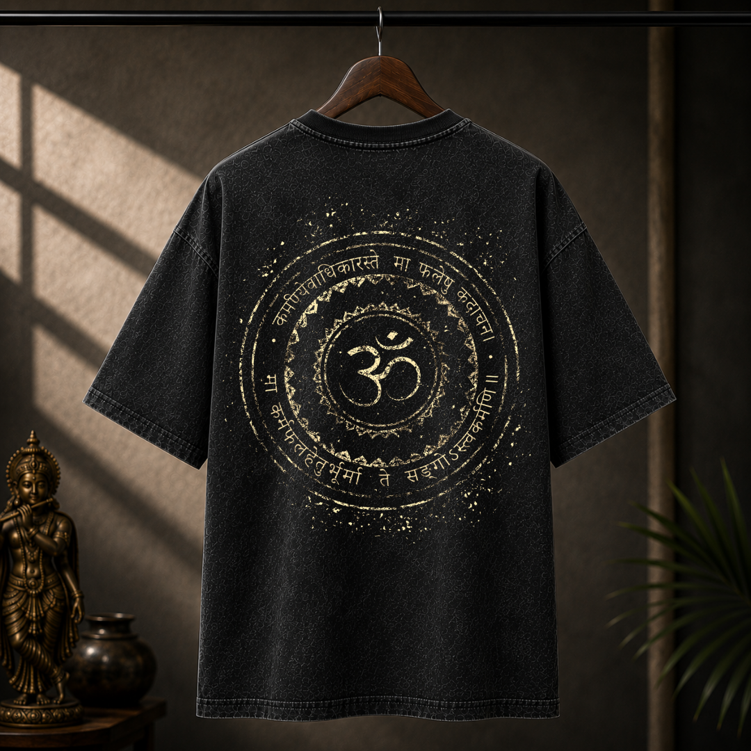 A black washed t-shirt hanging on a wooden hanger against a dark, atmospheric background with warm sunlight and shadows. The back of the shirt features a large distressed gold graphic with a central Om symbol and Sanskrit text.