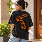 A woman wearing a black acid-wash graphic t-shirt with a large orange tiger design on the back, paired with light blue jeans, standing outdoors in front of a building with a wooden door.