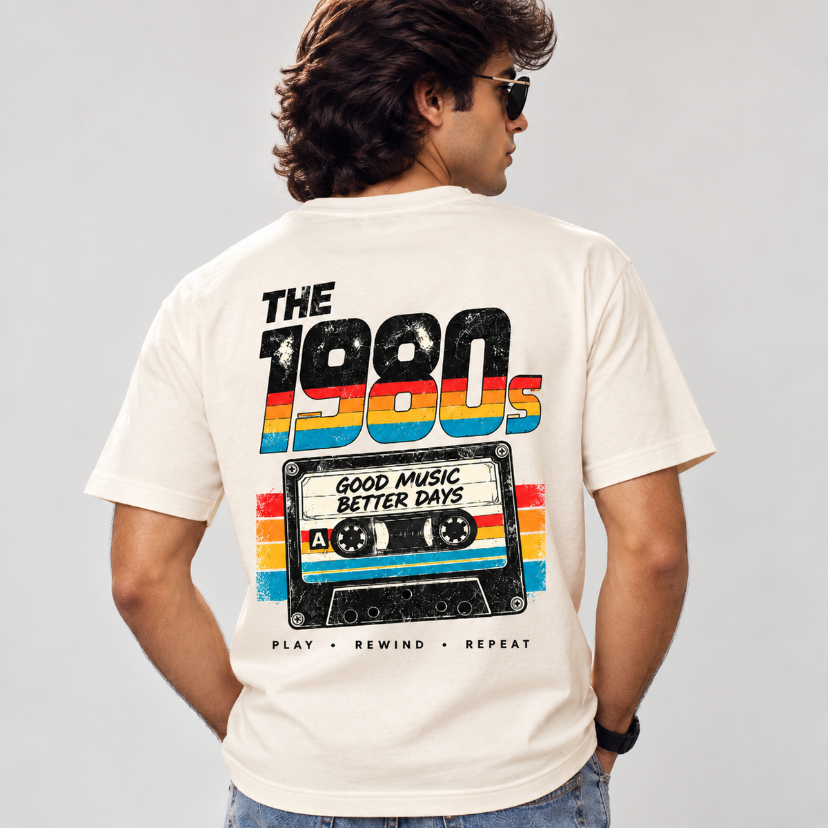 Back of off-white retro T-shirt worn by a man, with THE 1980s rainbow lettering and Good Music Better Days cassette graphic.