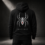 A person shown from the back wearing a black hoodie with a large white spider graphic and the word 'INSTINCT' on the back, standing against a dark concrete wall.