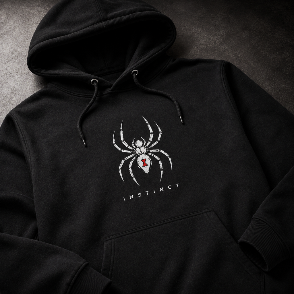 A black pullover hoodie laid flat on a dark textured surface, featuring a white spider graphic with a small red accent and the word 'INSTINCT' printed below.