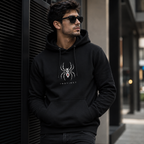 A man wearing a black pullover hoodie with a white spider graphic and the word 'INSTINCT' on the chest, standing outdoors against a dark modern building wall.