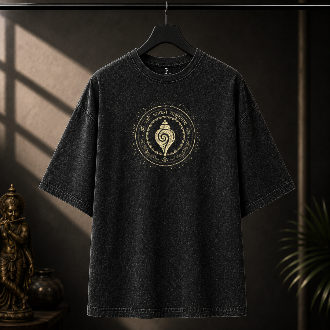 A dark washed black t-shirt hanging on a black hanger against a dark background with dramatic window shadows. The shirt features a circular gold graphic on the chest with a central spiral shell motif and decorative text.